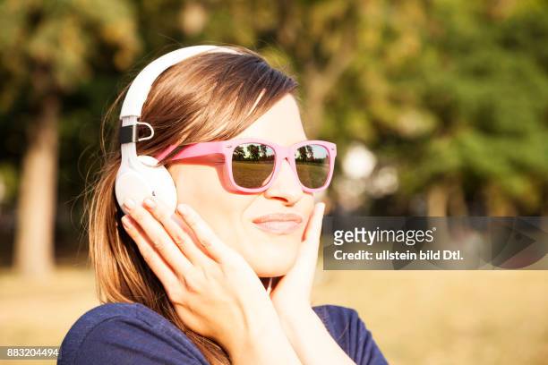 Frau mit Kopfhörern und Sonnenbrille im Park