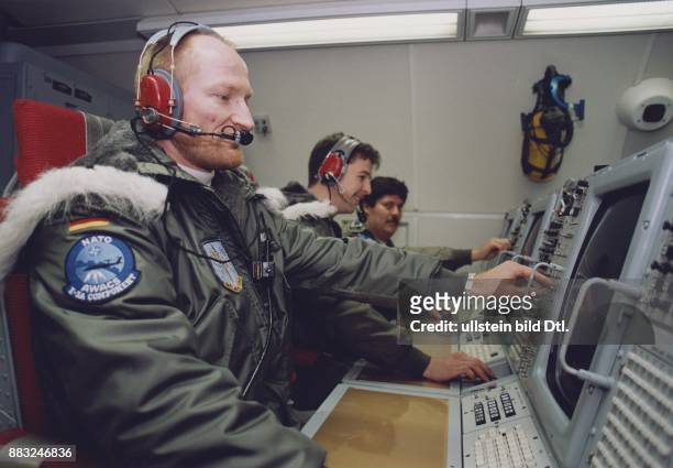 An der Schaltkonsole des fliegenden Frühwarnsystems der NATO AWACS sitzen drei deutsche Besatzungsmitglieder in grünen Militärjacken. Zwei von ihnen...