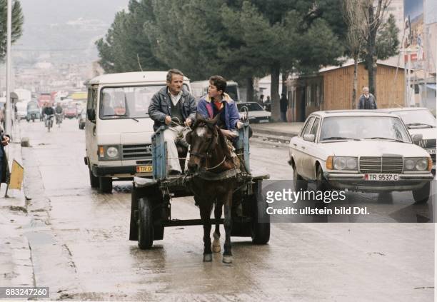 Tirana : Ein Pferdefuhrwerk fährt neben PKWs auf einer regennassen Straße der Hauptstadt. Straßenverkehr / Mercedes. .