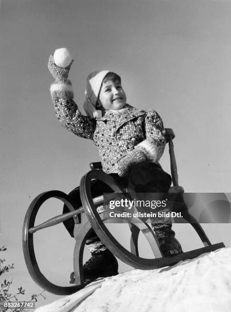 Ein Junge in einer Winterjacke auf einem Schlitten wirft mit einem Schneeball Aufnahme: Sonja Georgi Originalaufnahme im Archiv von ullstein bild