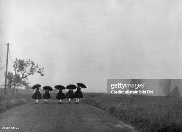 Frauen gekleidet in traditionellen Trachten auf dem Weg zu einem Volksfest bei Regenwetter Aufnahme: Tim Nachum Gidal Originalaufnahme im Archiv von...