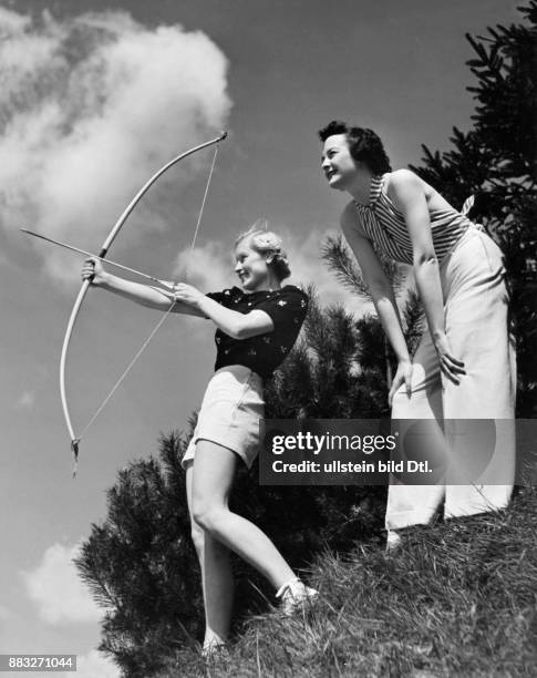 Zwei Models präsentieren Sommermode für Frauen beim Bogenschiessen, eine kurze Hose und eine lange Leinenhose mit einem rückenfreien Oberteil...