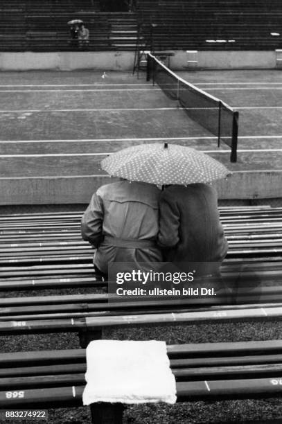 Zwei Menschen unter dem Regenschirm in den Sitzreihen auf dem Tennisplatz des Rot-Weiß Tennisclubs in Berlin Aufnahme: Hanns Hubmann Originalaufnahme...