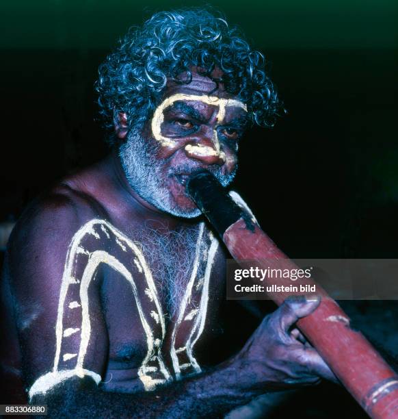 Aboriginal im traditionellen Corroboree Festschmuck blaest das Didgeridoo zum naechtlichen Tanz