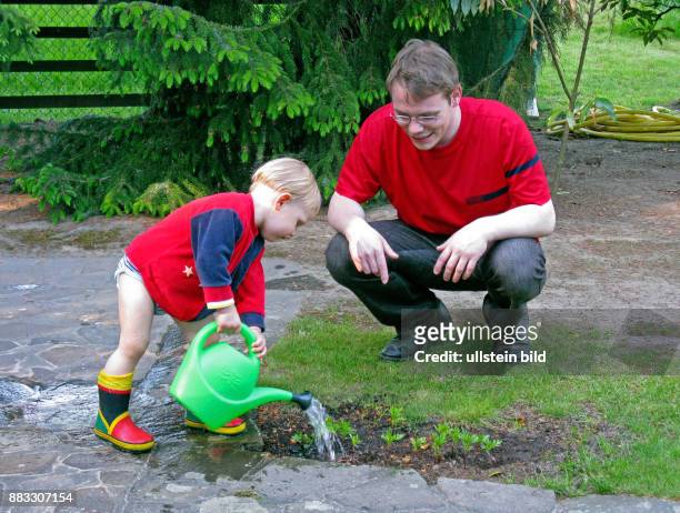 Junger Vater fuehrt seinen Sohn spielerisch an Pflanzen Garten und Natur
