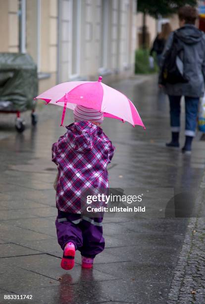 Ein kleines Maedchen mit Regenschirm in lila Winterkleidung