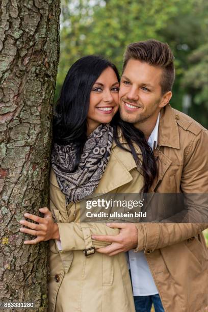 Ein junges, verlliebtes Paar schaut hinter einem Baum hervor