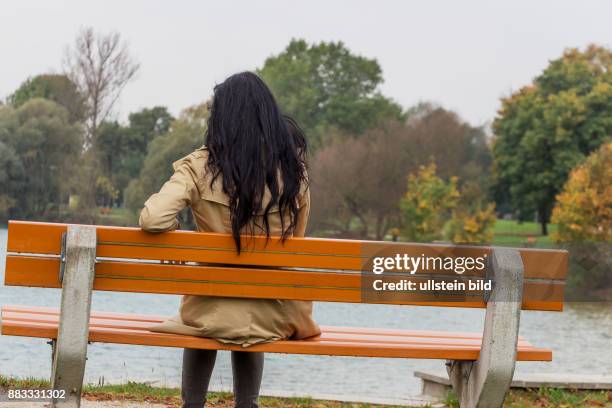 Eine junge Frau sitzt nachdenklich auf einer Parkbank