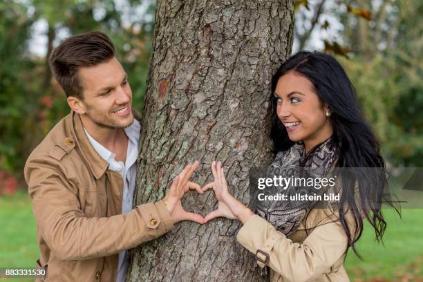 Ein junges, verlliebtes Paar schaut hinter einem Baum hervor