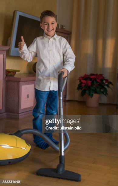 Ein Bub saugt mit einem Staubsauger ein Wohnzimmer. Kinder beim Putzen