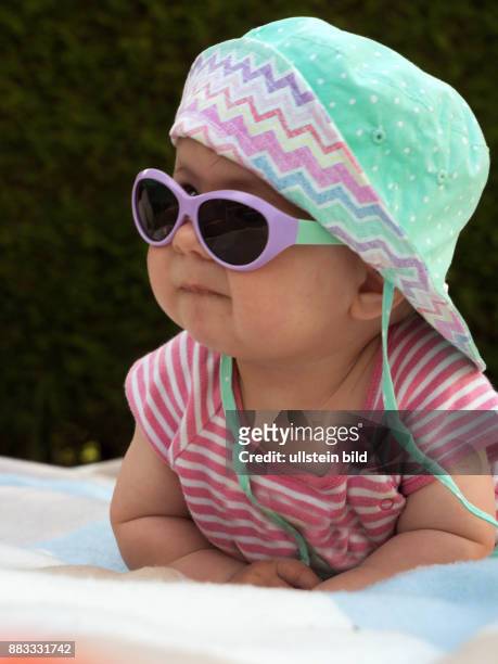 Ein Baby mit Sonnenbrille und Sonnenhut ist gut gegen die Hitze im Sommer ausgestattet
