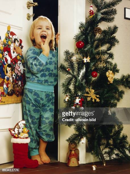 Nikolaustag: Ein Kind freut sich morgens über den mit Süßigkeiten gefüllten Stiefel vom Nikolaus. An der Tür hängt ein Adventskalender, an den...