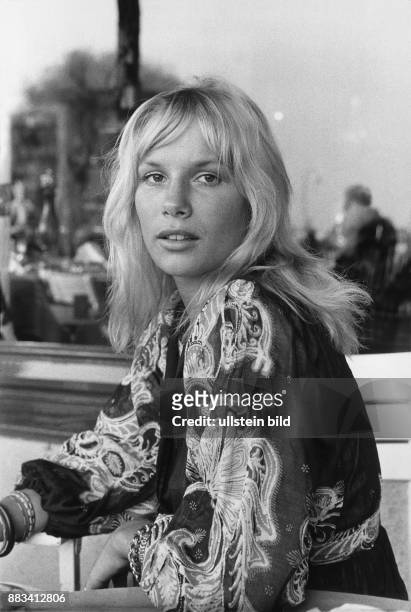 Die Schauspielerin Monique van de Ven trägt mehrere Armbänder und eine folkloristisch bedruckte Bluse im Stil der 70-iger Jahre. .
