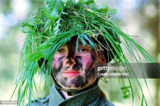 Weiblicher Soldat der Bundeswehr mit Gesichtstarnung und mit Gräsern getarntem Helm. .