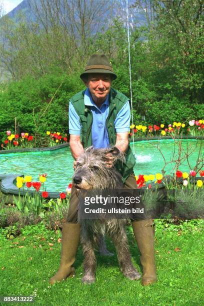 Der Theater- und Fernsehschauspieler Hans Clarin steht vor einem Teich seines Moserhofes in Aschau . Zwischen seinen Knien sitzt ein Irischer...