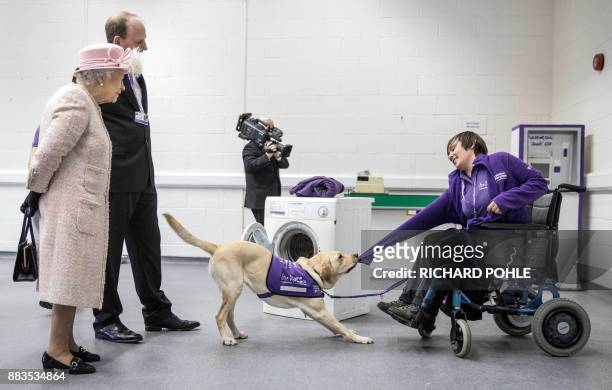 Britain's Queen Elizabeth II watches as 'Hettie' the Labrador dog demonstrates how she can help to undress a disabled person as she tours the...