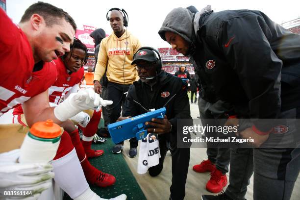 Brock Coyle, Reuben Foster and Linebackers Coach Johnny Holland of the San Francisco 49ers look over game images on sideline during the game against...