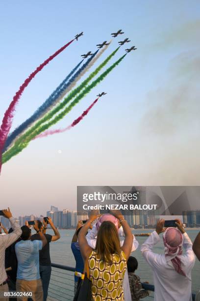 Spectators watch as UAE's Al-Fursan National Aerobatic Team performs with smoke along the corniche of the capital Abu Dhabi on December 1 during...