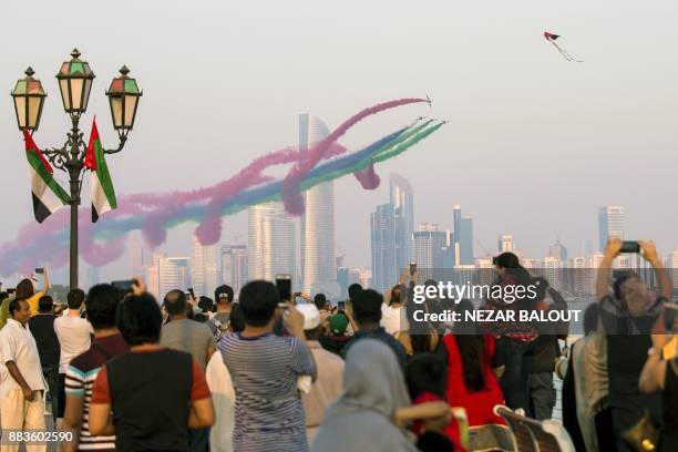 Spectators watch as UAE's Al-Fursan National Aerobatic Team performs with smoke along the corniche of the capital Abu Dhabi on December 1 during...