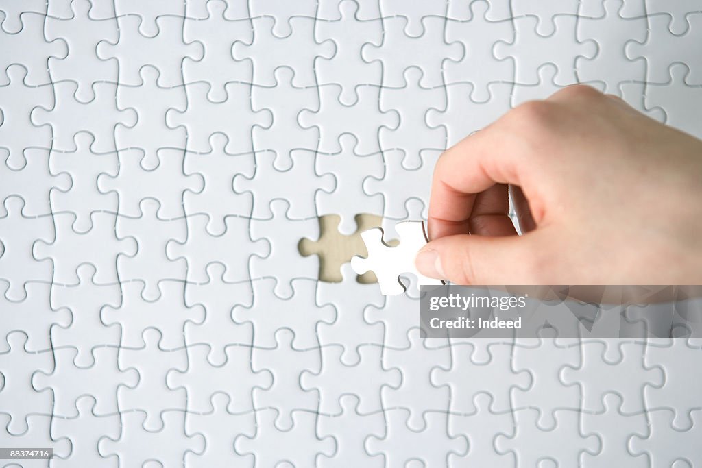 Hand placing last piece into blank jigsaw puzzle