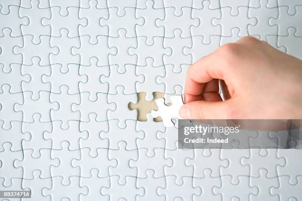 hand placing last piece into blank jigsaw puzzle - puzzle imagens e fotografias de stock