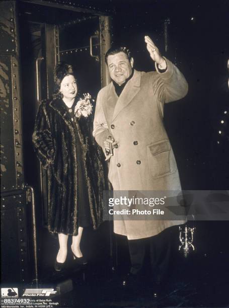 American baseball player George Herman 'Babe' Ruth , dressed in an overcoat, holds a cigar and waves as his wife, Claire Merritt Hodgson, in a fur...