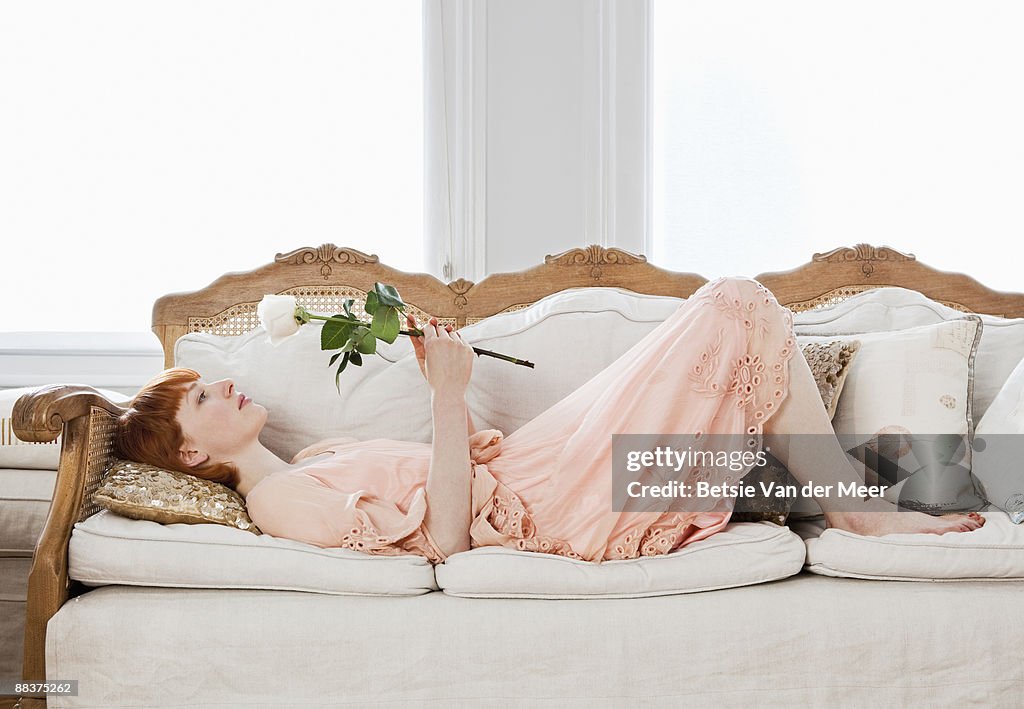 Woman resting on sofa looking at rose.