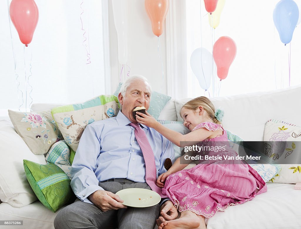 Young girl feeding cake to grandfather.