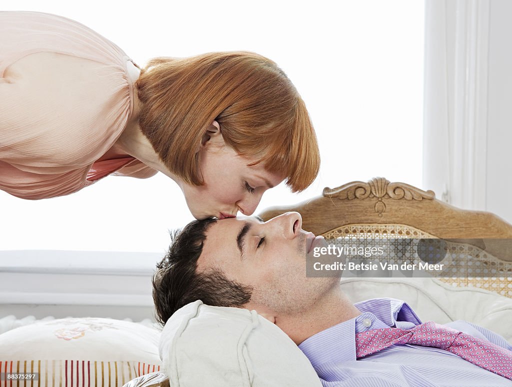 Woman kissing forehead of man resting.