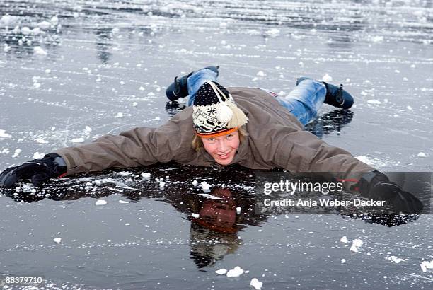 young male (16-17) in winter clothes lying on frozen lake, smiling - northern european descent ストックフォトと画像