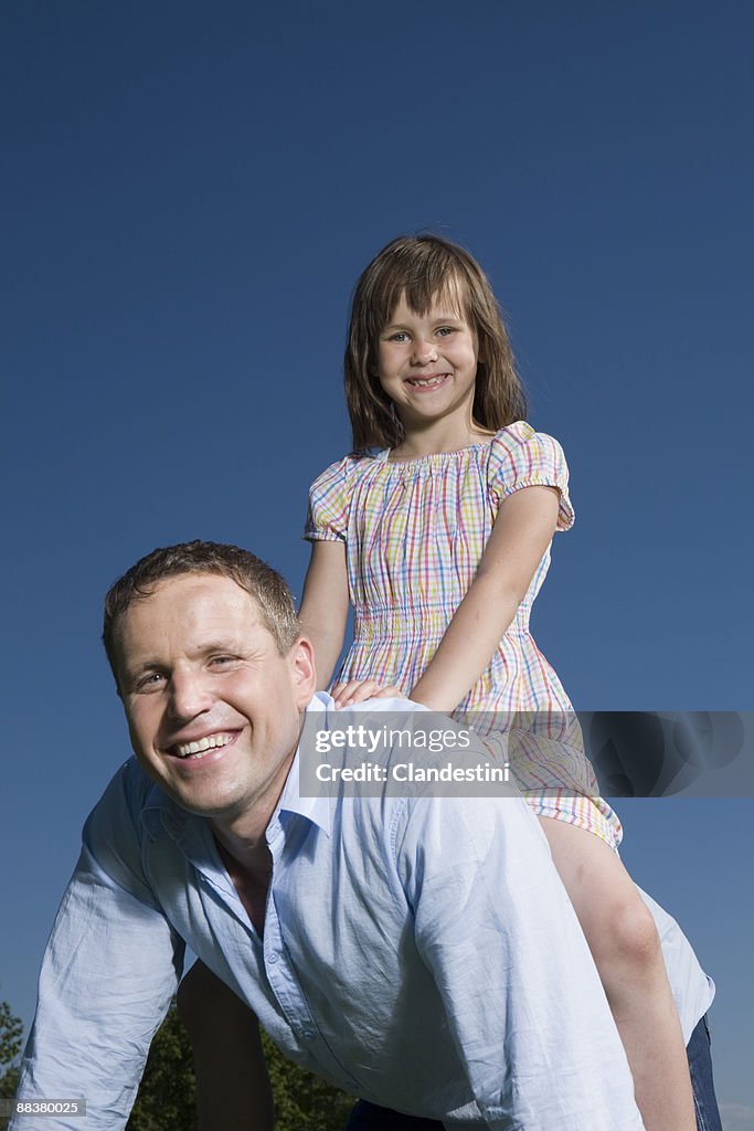 Little girl (6-7) sitting on father's back, smiling