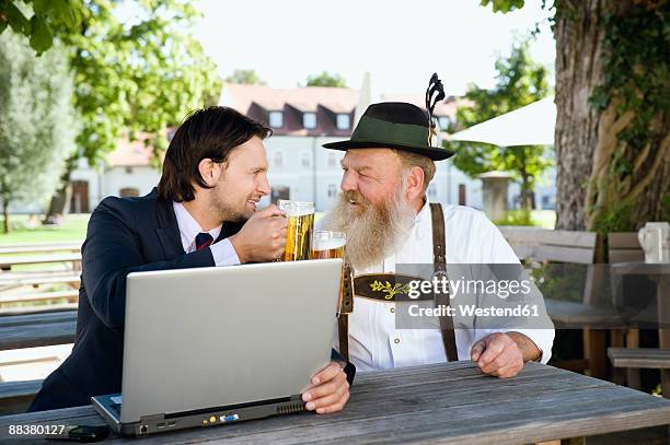 germany, bavaria, upper bavaria, senior bavarian man and young businessman with laptop in beer garden - knickers photos et images de collection