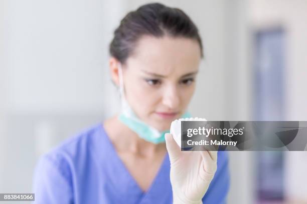 young dentist in blue scrubs and surgical mask examining a jaw model in the treatment room. - human jaw bone stock-fotos und bilder