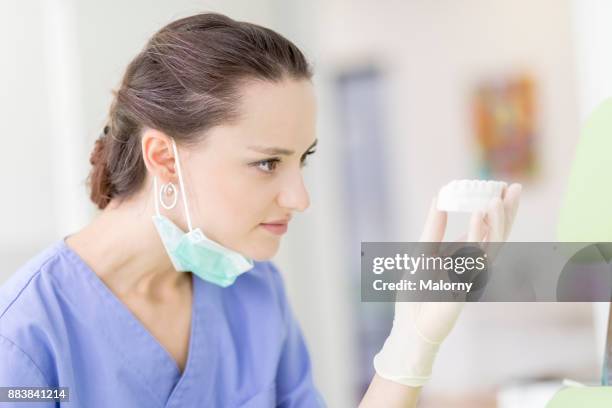 young dentist in blue scrubs and surgical mask examining a jaw model in the treatment room. - human jaw bone stock-fotos und bilder