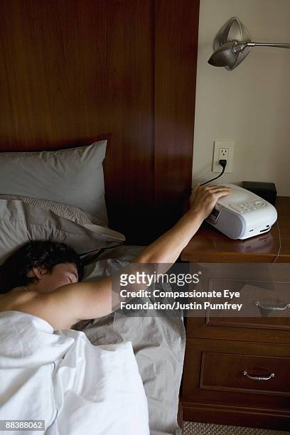 man in bed hitting alarm clock - colpire foto e immagini stock