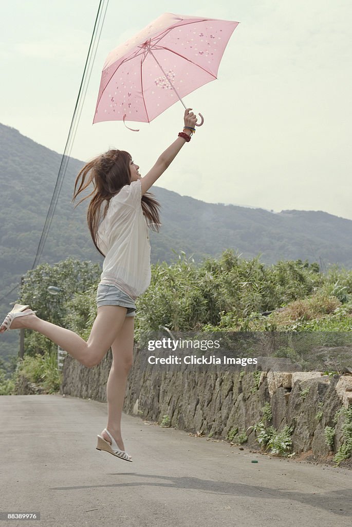 Girl holding an pink umbrella jumping