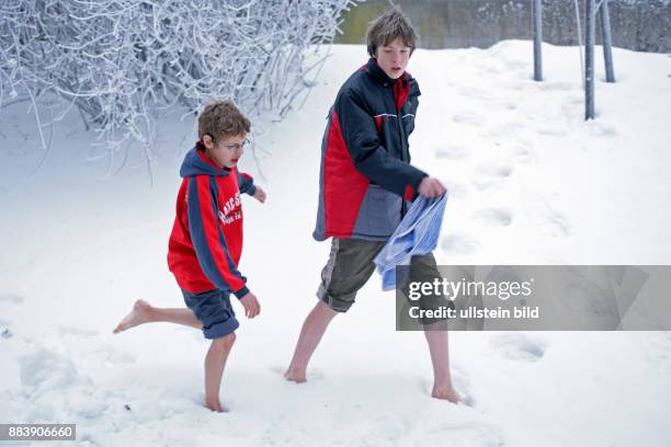 Two boys walking barefoot through snow