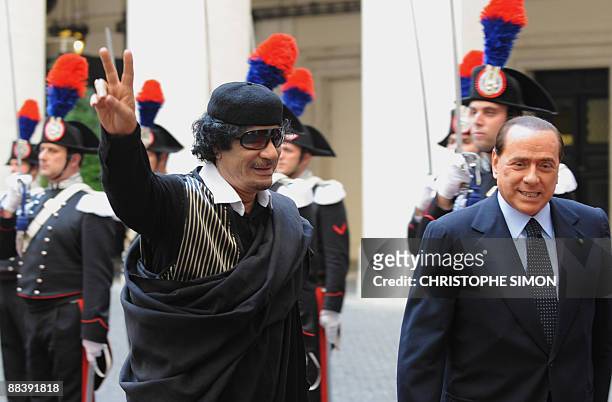 Libya's leader Moamer Kadhafi flashes a V-sign as he is greeted by Italian Prime Minister Silvio Berlusconi prior their meeting on June 10, 2009 at...