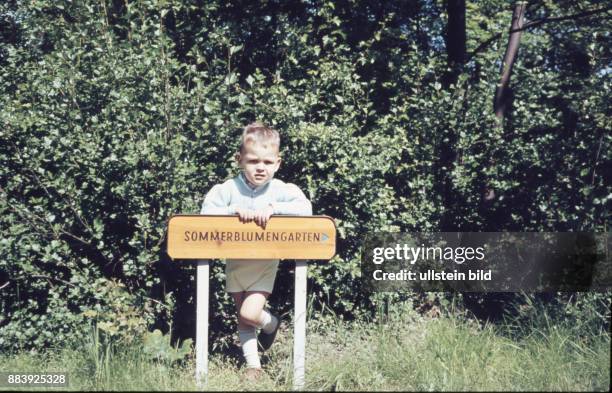 Aufnahme ca. 1950, Kindheit, ein Junge auf einer grünen Wiese lehnt an einem Schild Sommerblumengarten