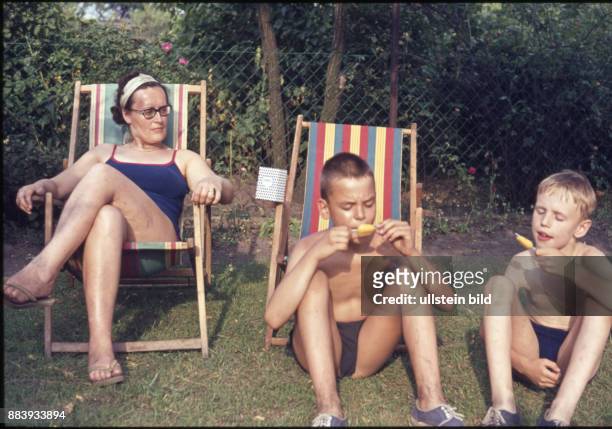 Ca. 1950, Kindheit, zwei Jungen und eine Frau sitzen im Garten, die Kinder essen Eis