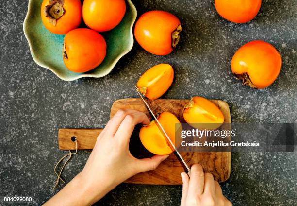 delicious fresh persimmon fruits. woman's hands cuting a persimmon, top view - caqui fruta tropical - fotografias e filmes do acervo