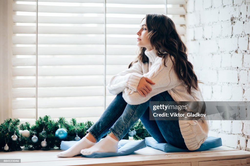 Young beautiful woman relaxing on window sill in christmas decorated home.