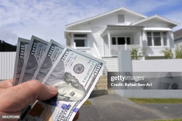 hand holds us dollar bills against a north american house - nz house and driveway stock-fotos und bilder