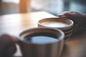 Close up image of two people clink coffee cups on wooden table in cafe