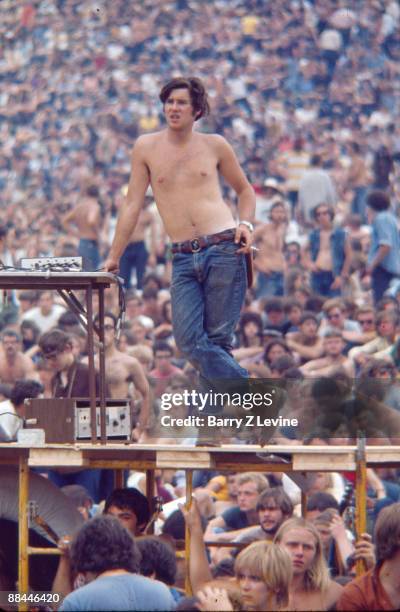 An unidentified, shirtless man stands next to the soundboard and a raised platform amid the audience at the Woodstock Music and Arts Fair in Bethel,...