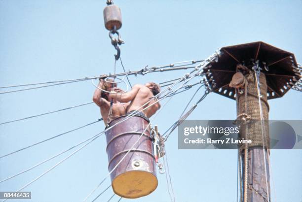 Two unidentified, shirtless men in a barrel suspended by a crane tighten cables above the stage at the Woodstock Music and Arts Fair in Bethel, New...