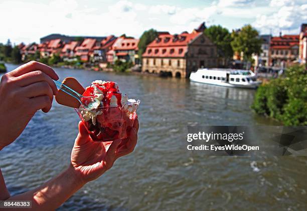 Person eating ice cream and a tourist boat on the river Regnitz on June 11, 2009 in Bamberg, Germany. Bamberg is listed as a World Heritage by UNESCO.