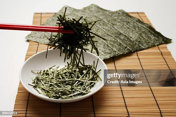 seaweed shreds picked up by red chopstick with seaweed sheets in background - red seaweed stock pictures, royalty-free photos & images