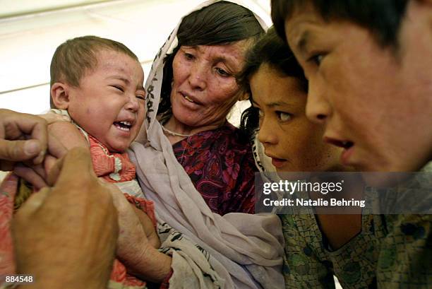 Family watches a baby receive a measles immunization shot at the Puli Charchi distribution center July 1, 2002 in Puli Charchi, Afghanistan. About...