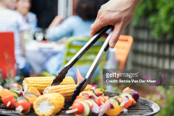 close up of hand turning corn on the barbecue, using servingtongs. - vegetarian stock-fotos und bilder